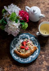 Green tea, strawberry crumb foccacia and a bouquet of summer flowers on a wooden background, top view