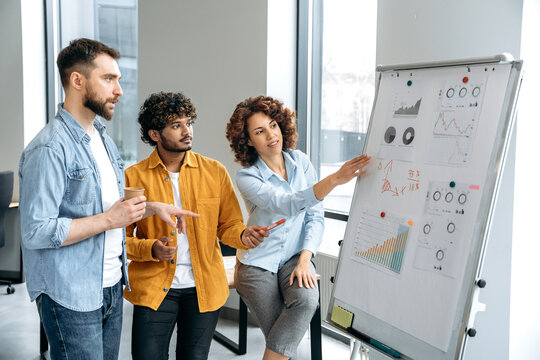 Teamwork. Successful multiracial colleagues, stand in the office near a marker white board, analyze the results of work, financial statistic, predict financial risks and profitability in a boardroom
