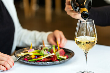 Waitress pouring white wine at table next to woman