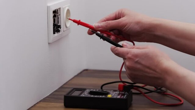 an electrician check a installed wall socket with a digital multimeter.