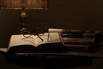 an antique lamp illuminates a table on which there are book and newspapers