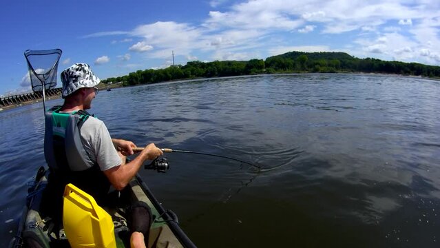 Wide angle head mount view of man catching catfish from kayak while fishing on the river.