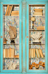 Vintage bookcase with transparent glass doors and antique books on the shelves.