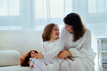 Portrait of happy family. Young mother and little daughter sits on a couch and having fun together at home.