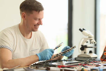 Smiling man studies broken motherboard in repair workshop