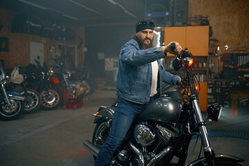 Handsome bearded man testing new motorbike in garage store