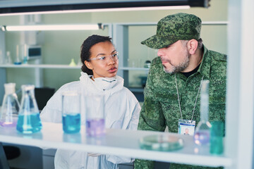 Young female chemist in coveralls and mature military man in uniform discussing new experiment...