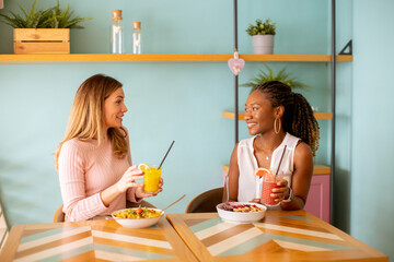 Young black and caucasian woman having good time, drinking fresh juices and having healthy...