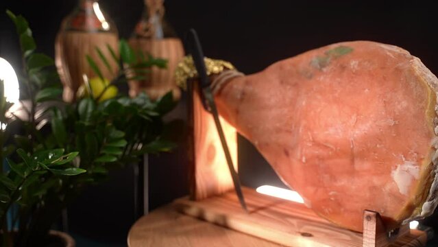 Traditional fat dry cured ham leg on wooden stand against rustic background, Italian salted prosciutto in typical grocery store, parma ham ready for slicing