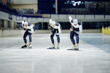 Front view of group of young sportsmen in uniform bending forwards while speed skating on ice rink during training or competition