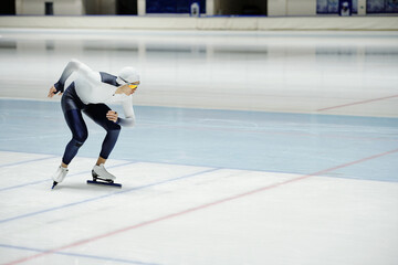 Young speed skater bending forwards while exercising on ice rink and practicing various positions while preparing for competition