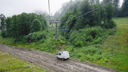 Early morning. The cable car with open empty cabins goes uphill. A car is driving down the road.