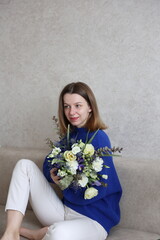 a beautiful girl in a blue sweater and white pants with a beautiful bouquet of flowers. International Women's Day.