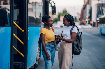 Couple of african american woman talking while waiting on a bus stop