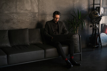 male businessman freelancer works in his office at a laptop on a leather sofa