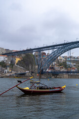 Imagen desde abajo del puente de Don Luis I  con un pequeño barco delante en el río de Oporto bajo un cielo nublado en un día de primavera.
