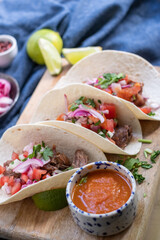 Freshly cooked tasty tortillas with fresh vegetables - red tomatoes, lettuce, red cabbage, lime juice. Tomato sauce in a porcelain blue-white dish on a wooden tray.