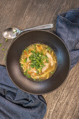 Fresh, freshly made appetizing chicken soup with greens in a beautiful black deep plate on a gray blue napkin. Placed on a wooden brown table.