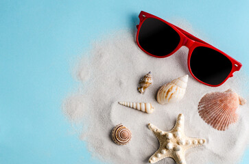 Sunglasses and sea shells on clean sand on a blue background.