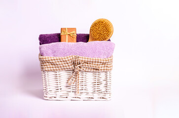Colored terry bath towels, soap and a dry massage brush in a basket on a white background.