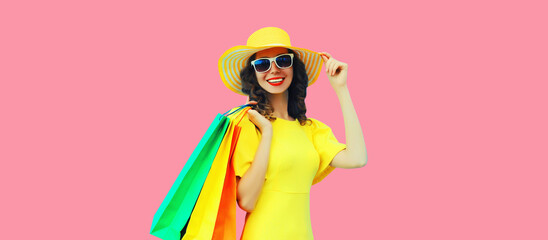 Portrait of beautiful happy smiling young woman with shopping bags wearing yellow dress and summer straw hat on pink background