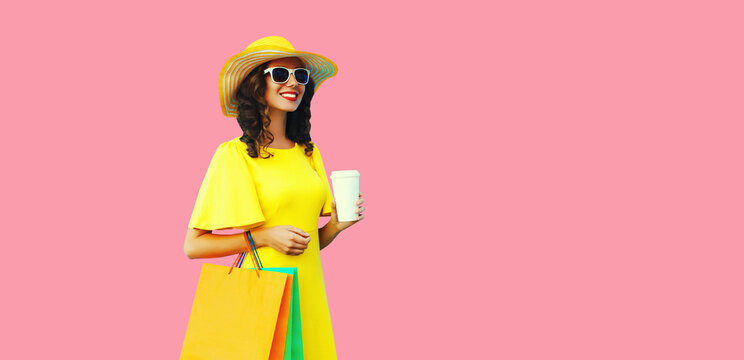 Portrait of beautiful happy smiling young woman with shopping bags wearing yellow dress and summer straw hat on pink background