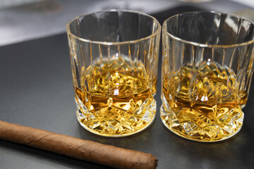 Two glasses of whiskey and a cigar on a black background.