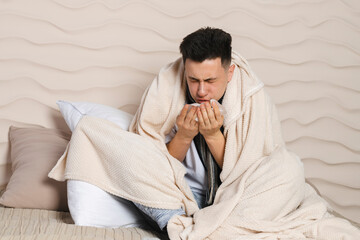 The young man is lying in bed wrapped in a blanket and is sick with a cold, with a red face from...