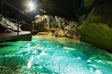 Dark cave view from inside with a lumen. Stalactites and stalagmites inside the stone grotto. Colorful stones in the cave. Lighting electricity beauty of the cave.