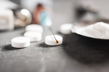 Drop of narcotic substances on a syringe needle, white pills and drugs powder, extreme close-up view. Concept of addiction and bad habits