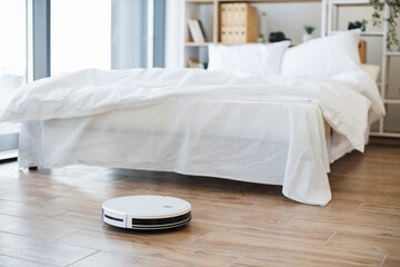 Efficient robotic vacuum cleaner removing dust from hard flooring against cozy sleeping room...