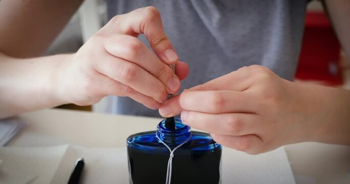 Front view of woman pumping blue luxury ink inside fountain pen right after unboxing