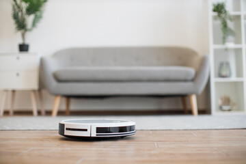 Automatic robot vacuum moving from soft carpet to hardwood floor while removing dust in living room. Smart home device conducting daily vacuuming and saving residents from seasonal allergies.