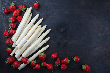 Reife rote Erdbeeren und Spargel aus biologischem Anbau angeboten als Draufsicht auf einem rustikalen schwarzen Board mit Textfreiraum rechts