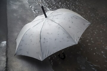  a white umbrella sitting on the side of a wet road next to a street curb with water droplets on the ground and a black handle on the umbrella.  generative ai