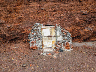 Old door in the famous Red Beach, Kokkini Paralia in Santorini island, Greece. Unique red sand beach on a cloudy day
