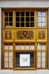 Ornate gold window set in commercial building with wall of white marble - sign mounted in window says Lets make a PLAN together