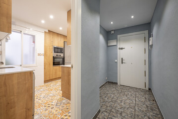 Entrance hall of a house with access to a kitchen with wood-colored furniture and hydraulic stoneware floor