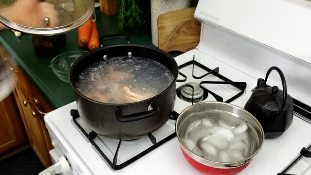 Checking and string shrimps while being cooked in pot of hot water over gas stove while bowl of ice water prepared for cooling down sea food.