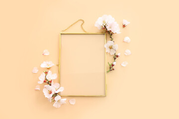 top view of almond blossom tree flowers and gold elegant empty frame over yellow pastel background. For mock up, copy space
