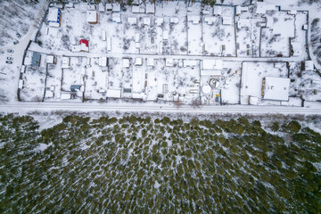 Aerial view of coniferous winter forest and a small houses.. Flying above frozen trees and snow...