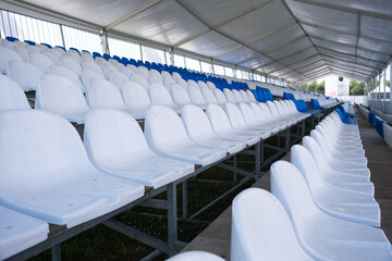 Empty white seats of tribune on sport stadium. Many empty plastic seats in rows in an outdoor stadium. Concept of fans, chairs for audience