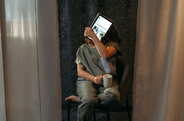 Portrait of a young woman who covers her face with a tablet