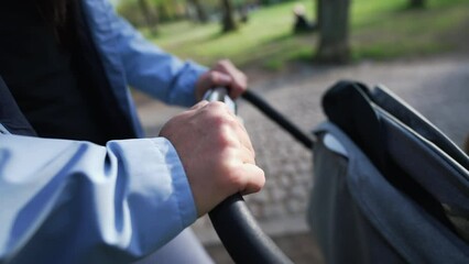Mother pushing baby carriage closeup hand holding stroller handle. Parent strolling outside at park during sunny day