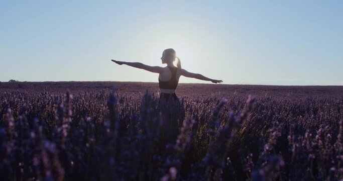 Dreamy girl in sports wear practices meditational yoga asanas in lavender fields at sunrise, inspiring wanderlust. Warrior pose practice. Stretching exercises. Healthy lifestyle blogger or model. 