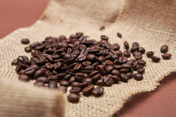 Fototapeta na wymiar Roasted coffee beans on the rural rough sackcloth and the bright solid fond plain brown background