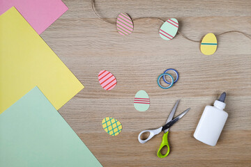 Process of creating Easter garland with decorative eggs. Flat lay. Colored paper for creativity,...
