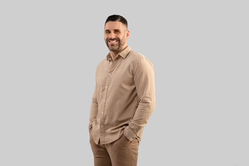 Fototapeta premium Portrait of positive middle aged man in shirt posing with hands in pockets smiling at camera, grey background