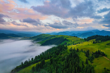 Fototapeta na wymiar Mountains in clouds at sunrise in summer. Aerial view of mountain peak with green trees in fog. Beautiful landscape with high rocks, forest, sky.