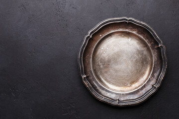 Empty vintage silver plate on black stone background. Top view with copy space